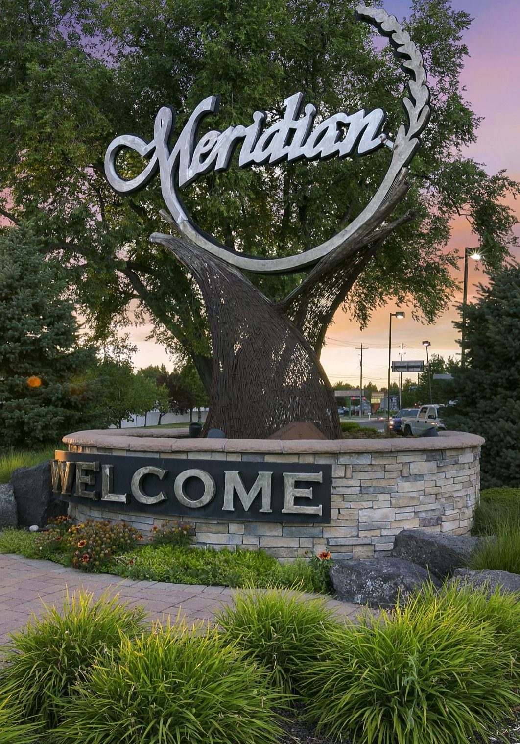 Meridian Idaho Welcome sign at an angle. Large tree behind sign with sunset peeking through