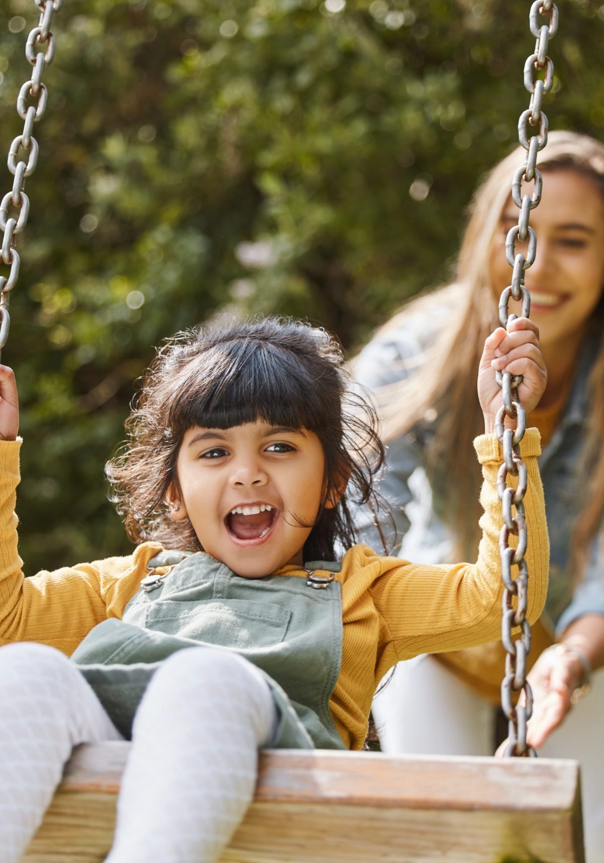 Happy, swing and mother and child in park for playing, bonding and having fun together outdoors. Nature, weekend and mom push little girl in playground for relaxing, childhood and happiness in summer.